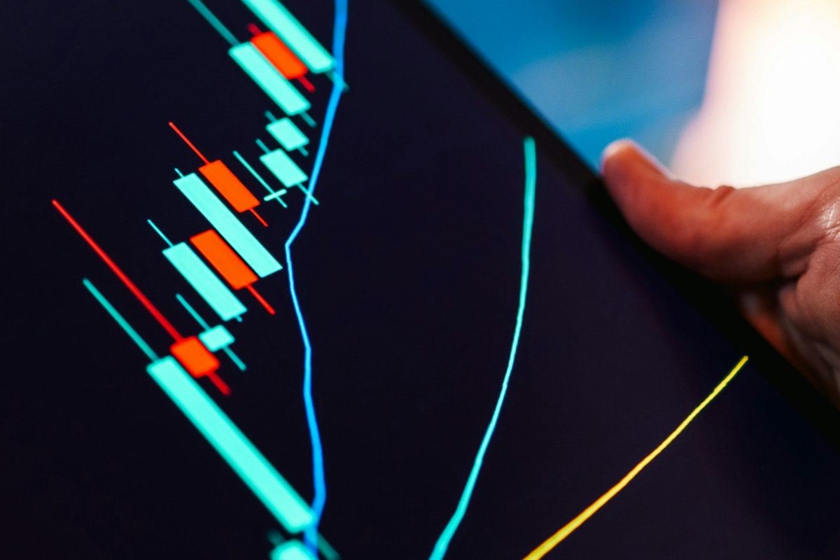 Hand holding tablet showing stock market candlestick chart