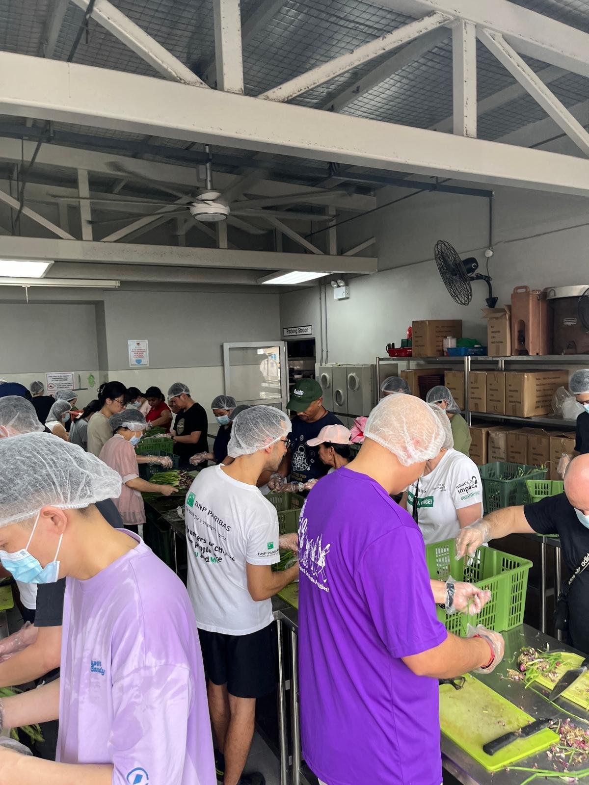 Volunteers in hairnets and gloves prepare and pack fresh produce at a community food-packing station