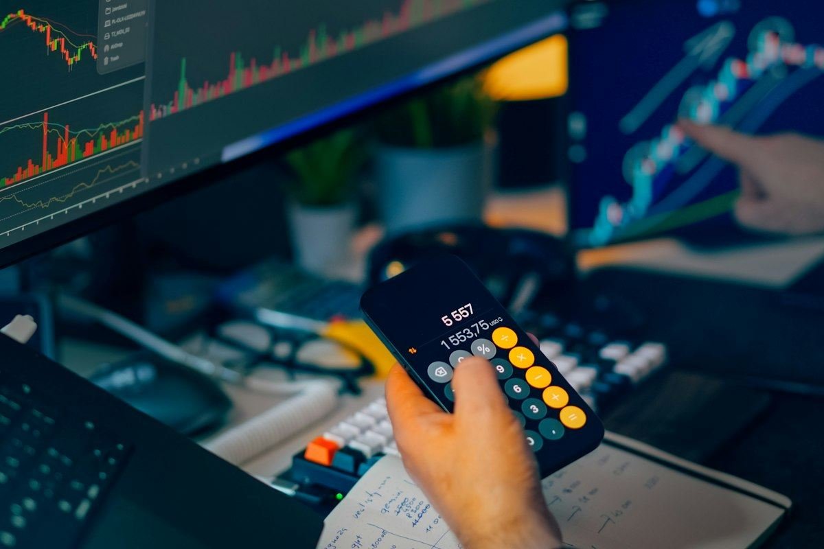 Trader analyzing stock market charts on computer screens with calculator