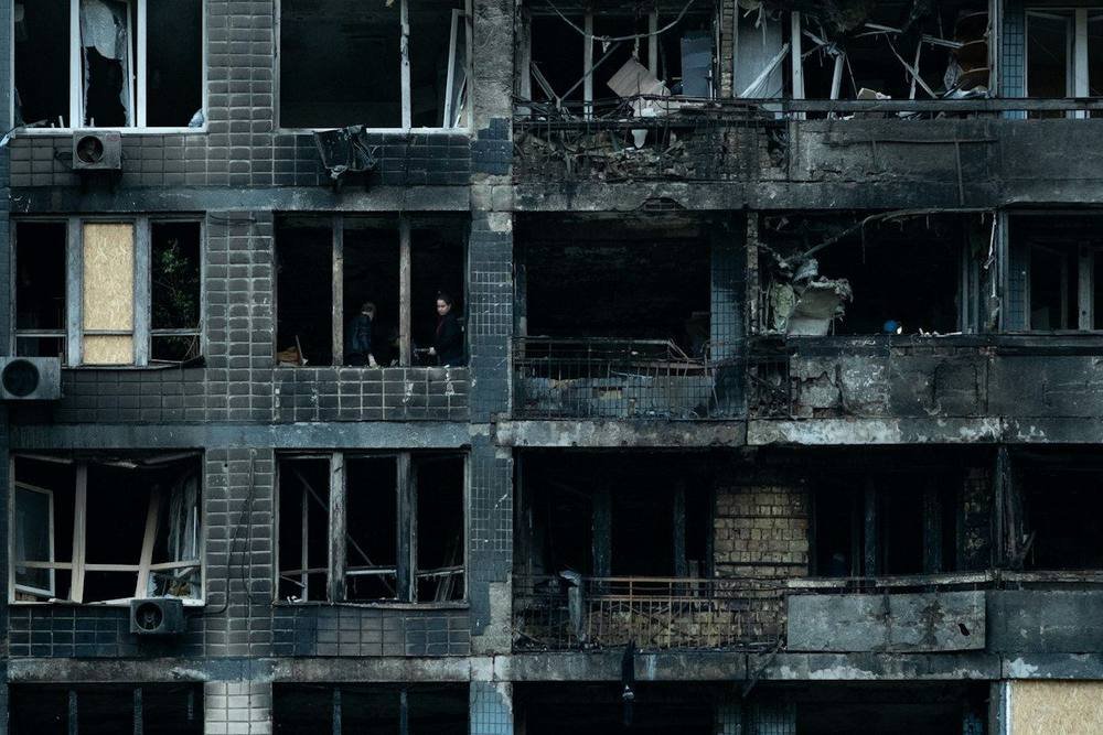 Damaged apartment building with boarded windows and debris